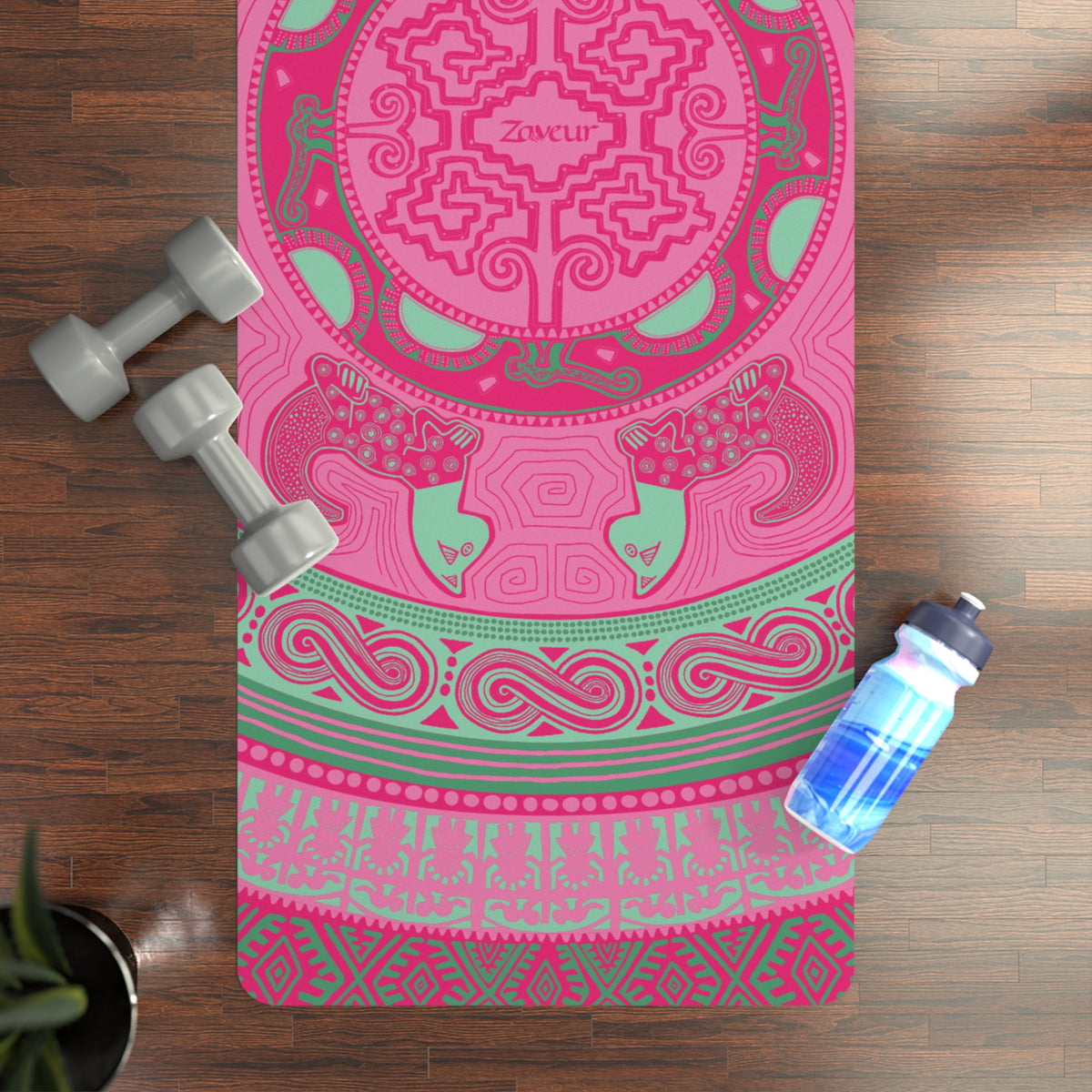 Colombian Dreams pink mandala yoga mat with Zaveur logo on a wood floor next to gray dumbbells and a water bottle
