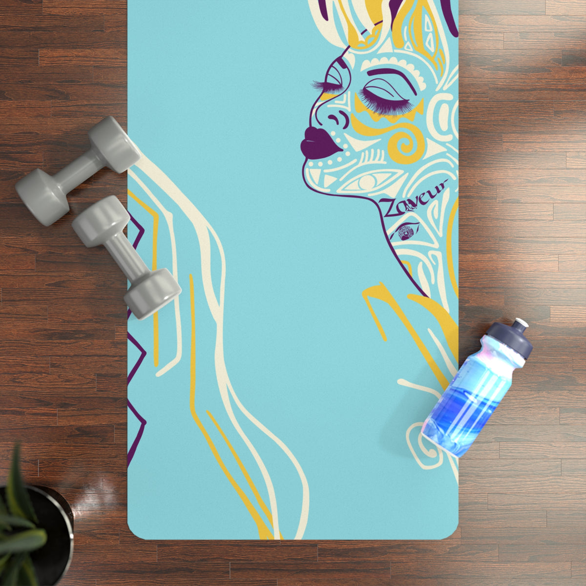 Queen of Phoenix turquoise yoga mat with line-art face on a wood floor next to gray dumbbells and a water bottle