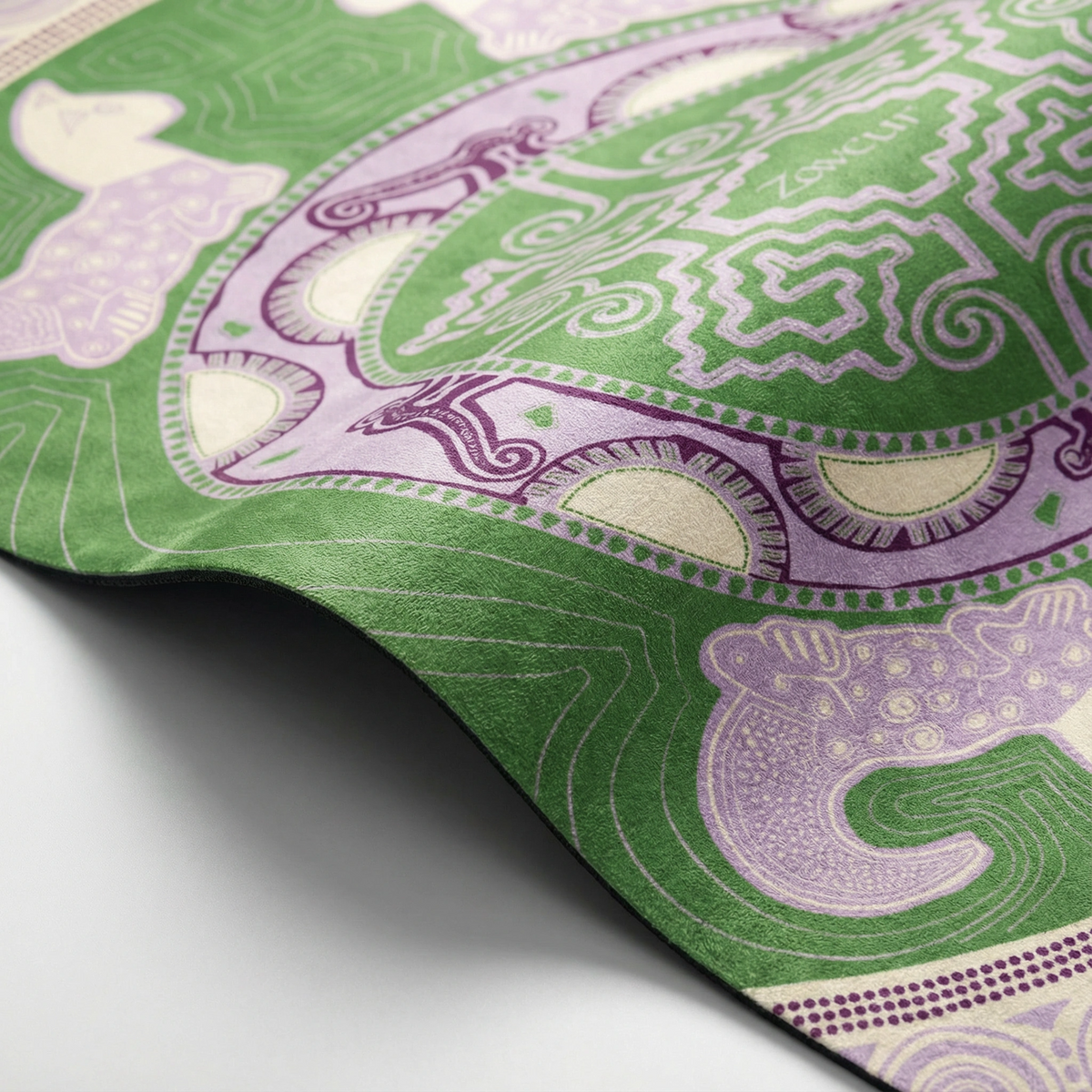 Corner of the green Colombian Dreams yoga mat curling up, a lilac cat figure and purple mandala ring up close