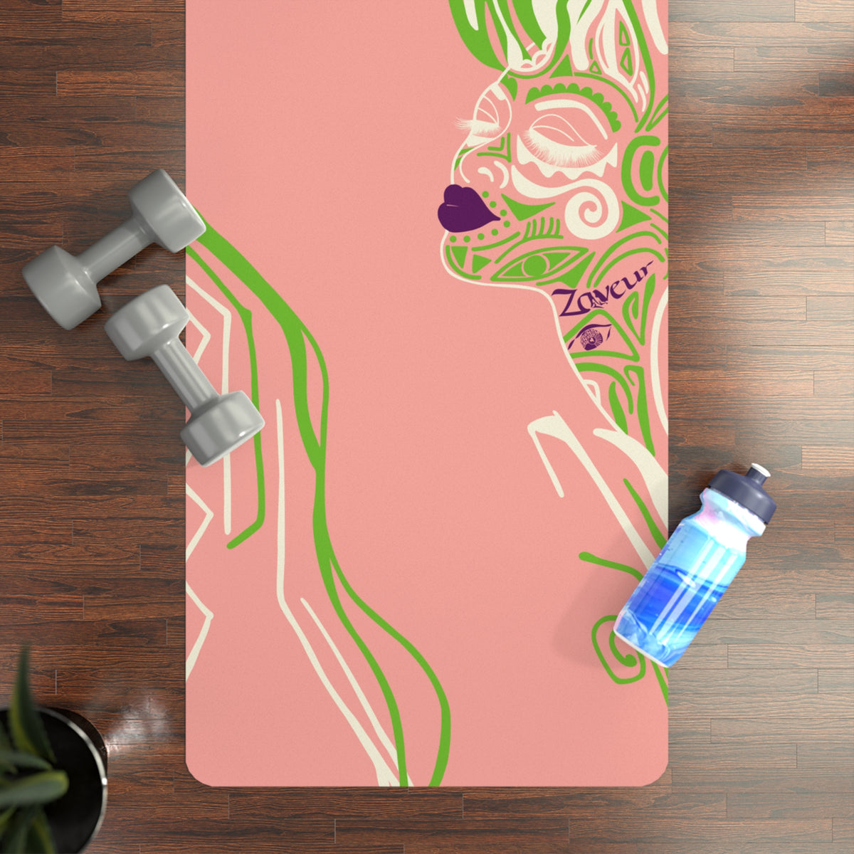 Queen of Phoenix pink yoga mat with green line-art face on a wood floor beside dumbbells and a bottle