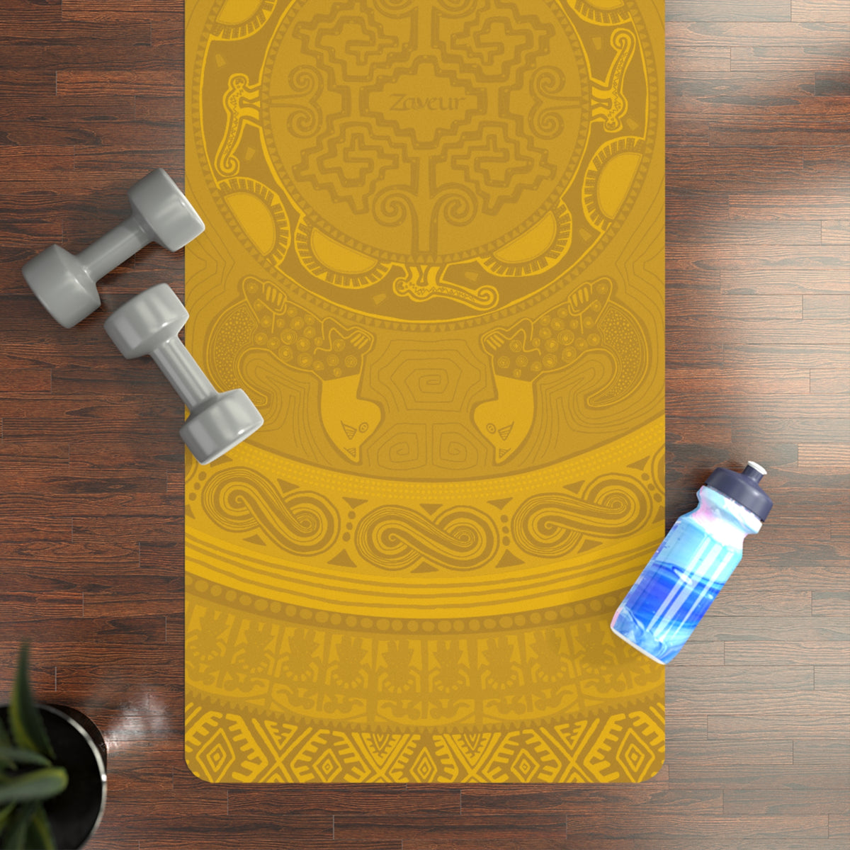 Colombian Dreams golden mandala yoga mat with Zaveur logo on a wood floor beside gray dumbbells and a water bottle