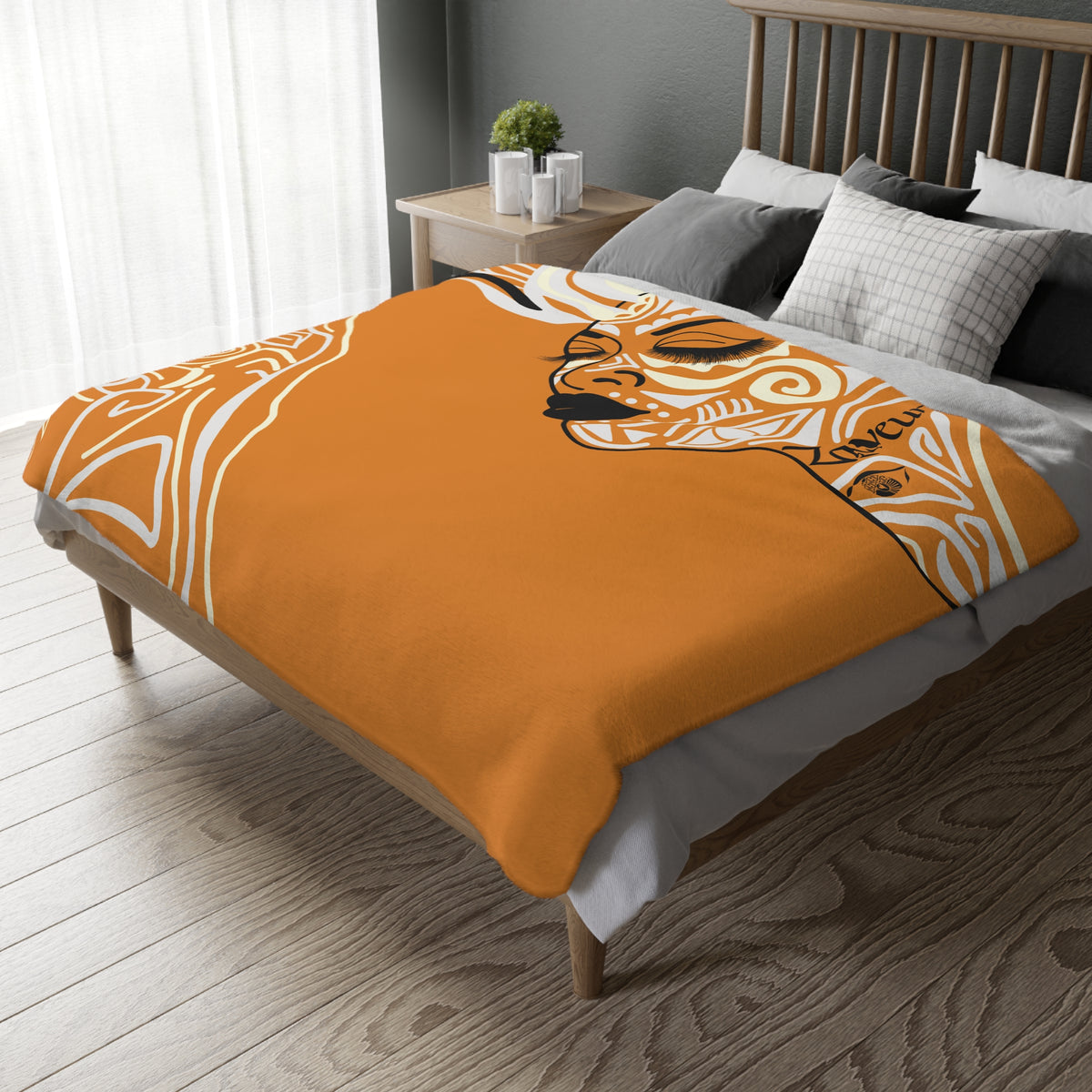 Orange Queen of Phoenix blanket with cream and black illustrated face profile draped over a wooden bed