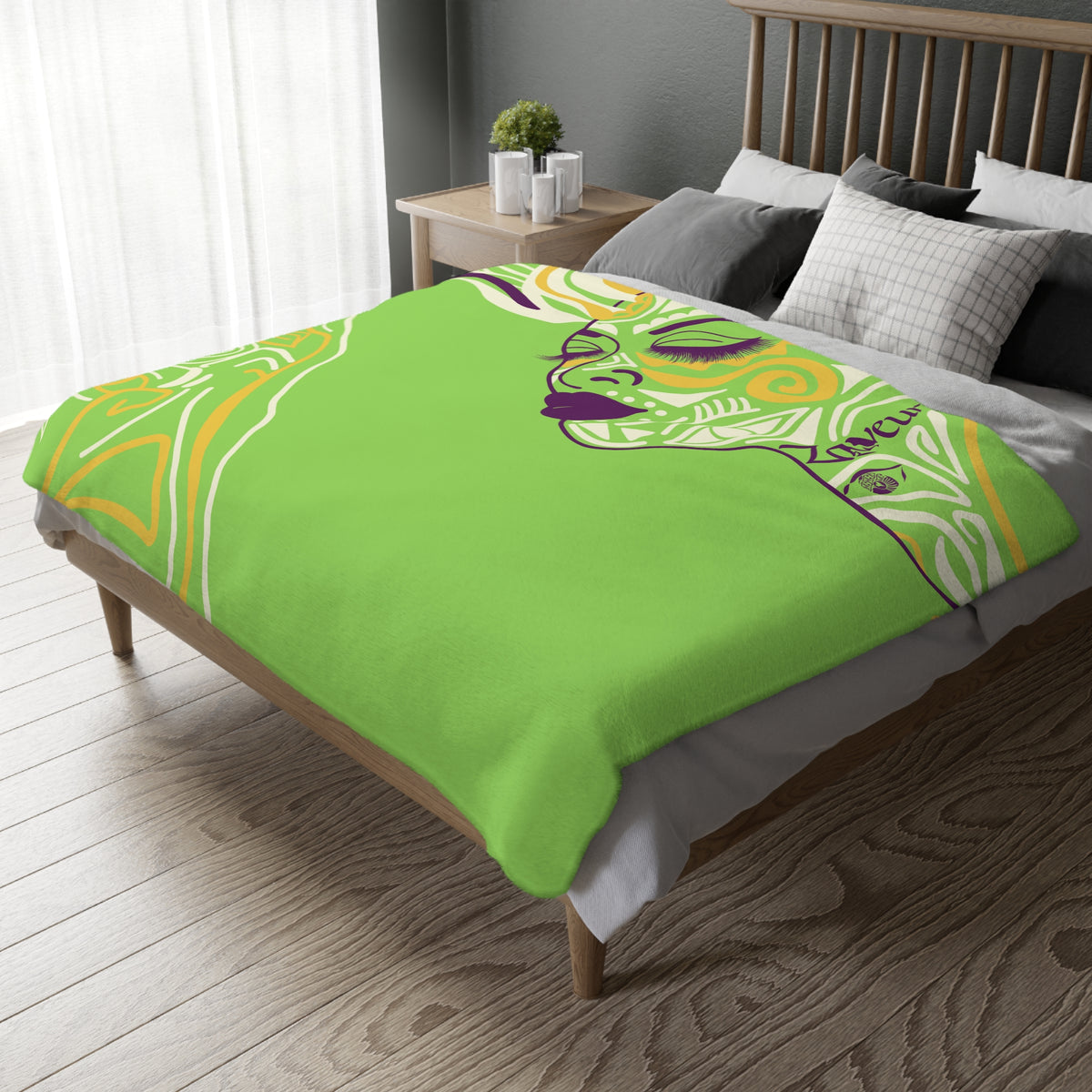 Queen of Phoenix green blanket with illustrated line-art face and gold geometric pattern draped over a wooden bed