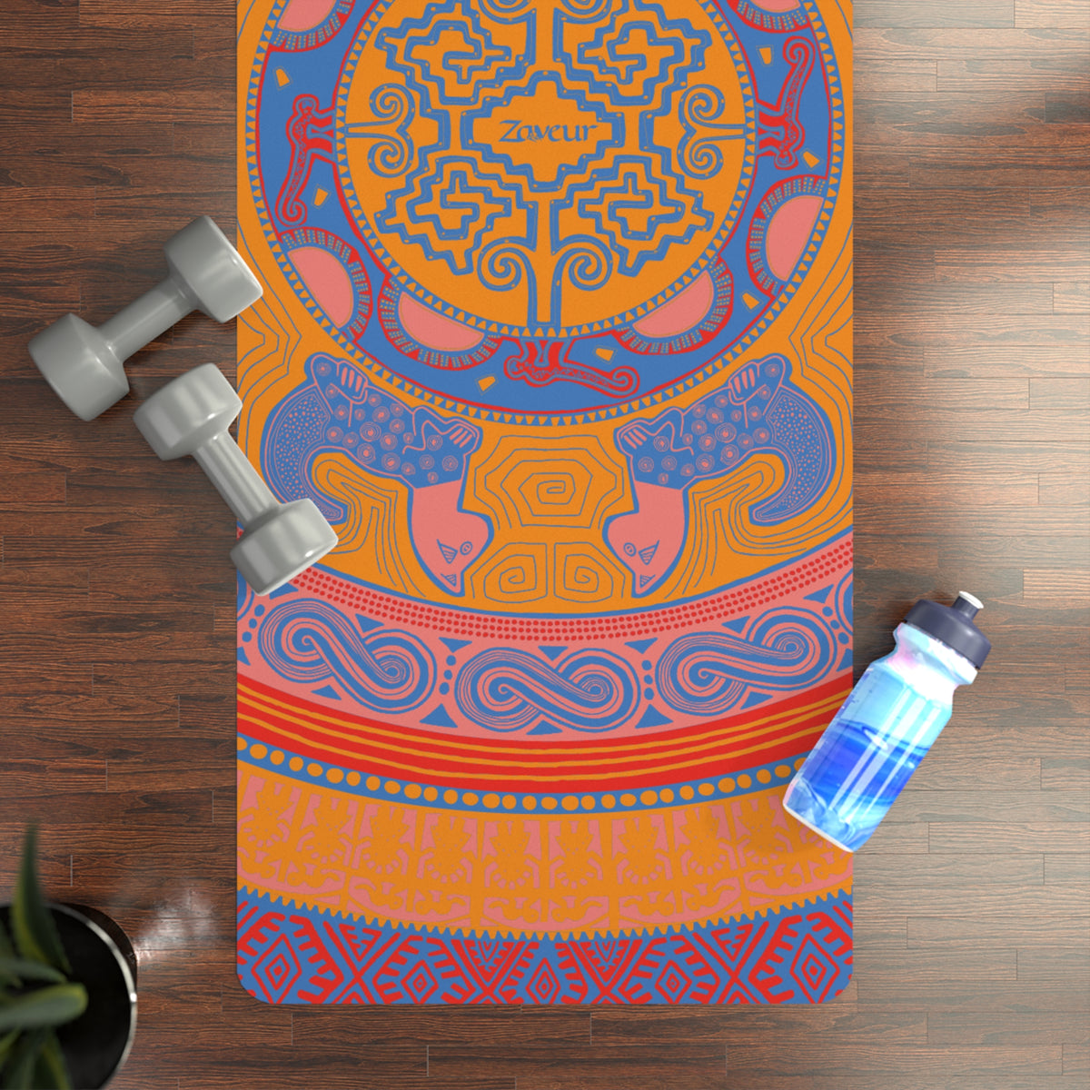 Colombian Dreams Mandala Tigers yoga mat in orange, blue and coral on a wood floor with dumbbells and a water bottle