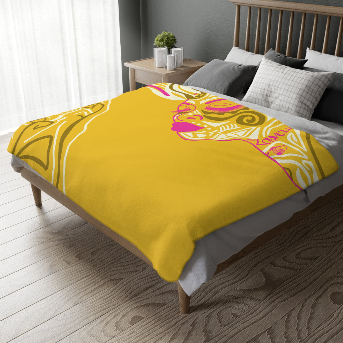 Queen of Phoenix yellow velveteen blanket with pink and white line-art face spread over a wooden bed in a bedroom