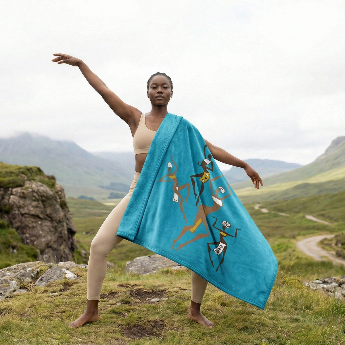 Woman in a dance pose on a mountain trail with the turquoise Dancing Ladies blanket over one arm