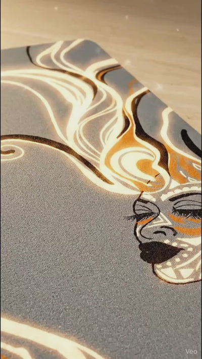 Queen of Phoenix yoga mat video: the slate grey mat on a stone floor, light tracing its line-art face and hair